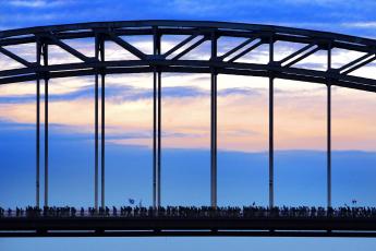 Wandelaars lopen in alle vroegte over de Waalbrug.